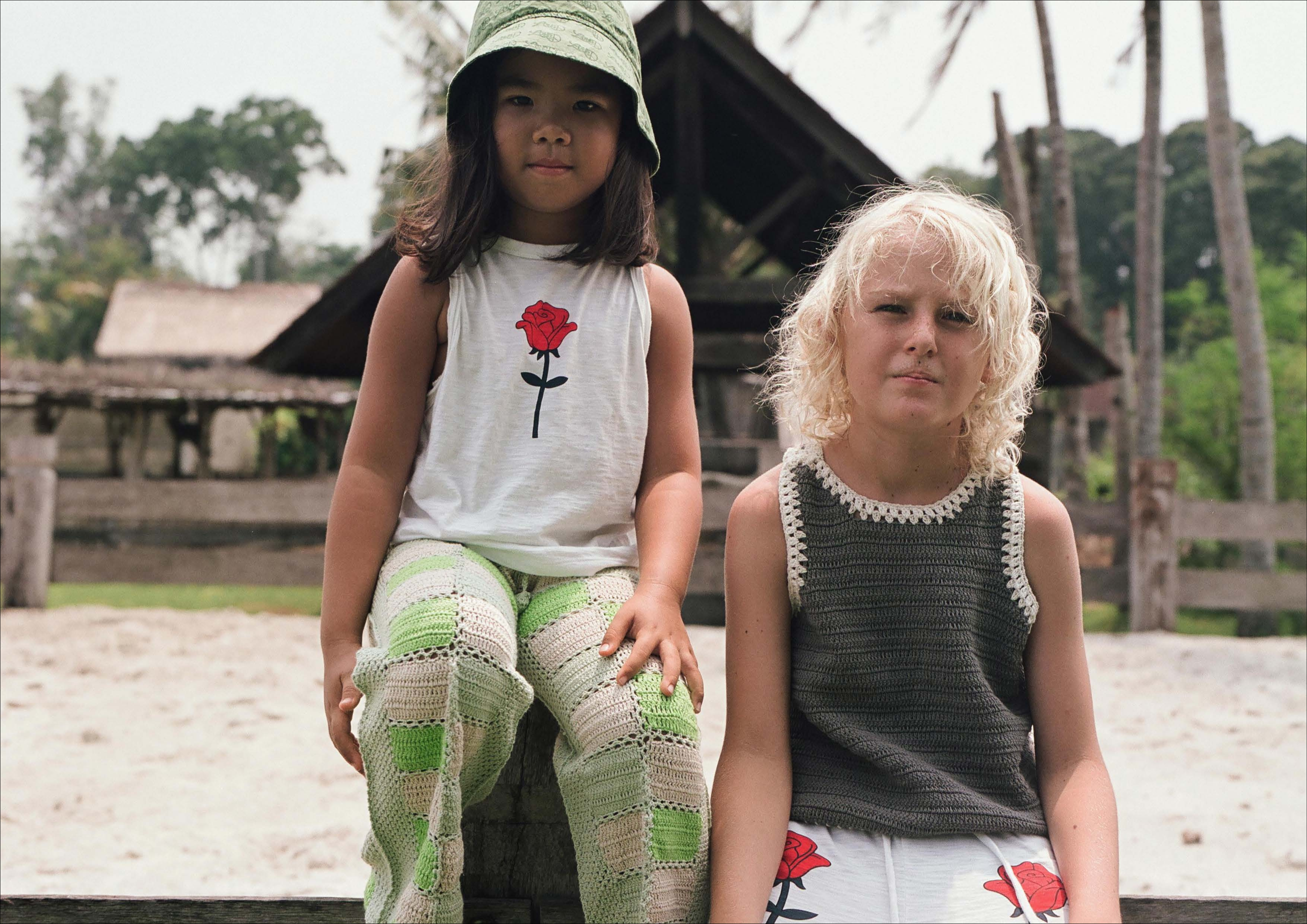 Two kids sitting side by side in patterned pants and summer tops